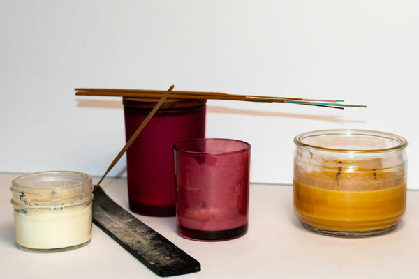 Assorted candles in various states of failure: tunneling soy candle with lavender bits, sooty wax tumblers, a layered candle with discolored streaks, and a burnt wood wick lying in the foreground.