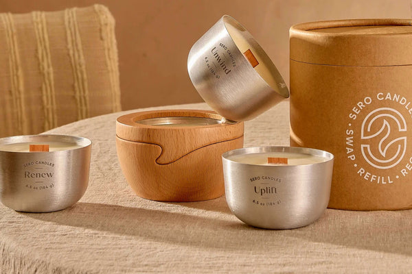 A Sero Starter Set on a linen table: two aluminum candle inserts, a beech wood holder, and the kraft tube printed Swap, Refill, Recycle.