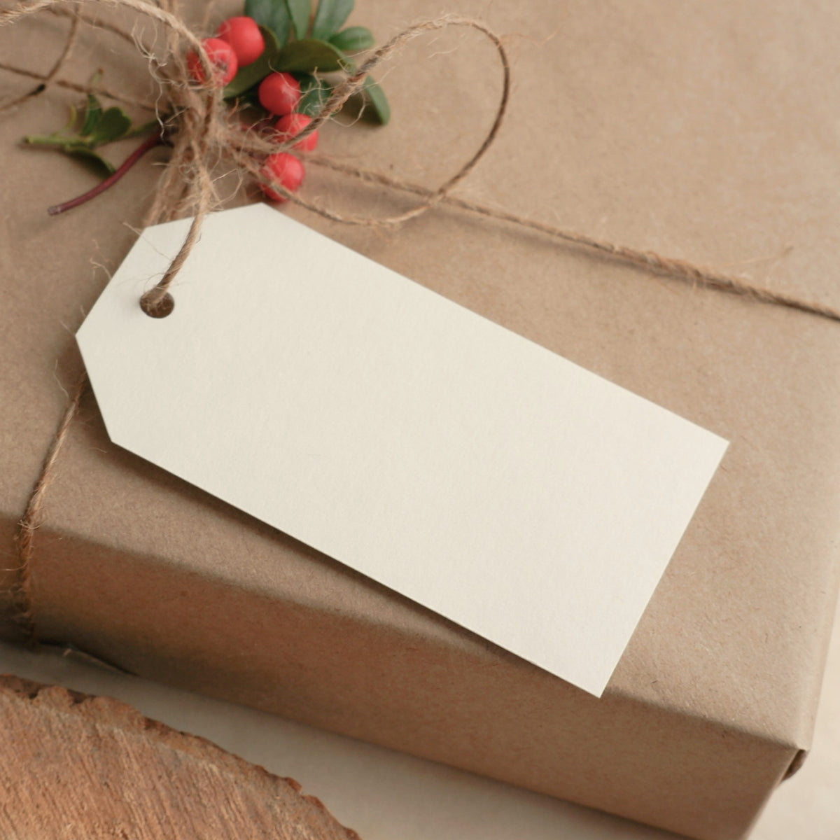 A gift wrapped in kraft paper and twine with a blank cream tag and a sprig of red berries