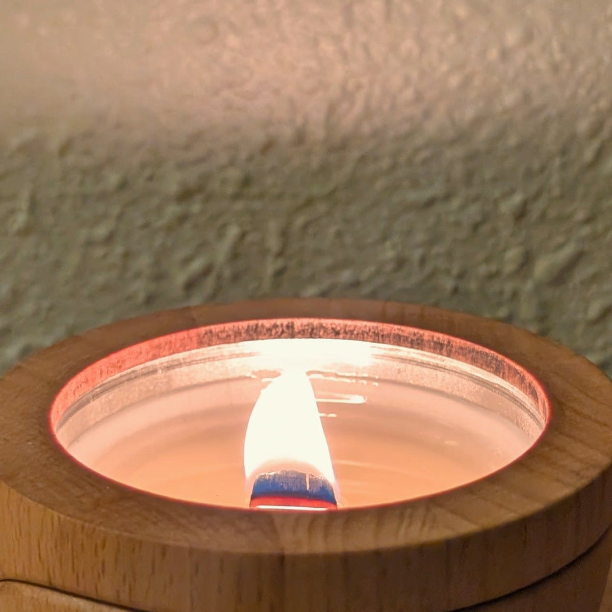 A Sero candle burning in its beech wood container on a bedside table, wick trimmed and flame steady.