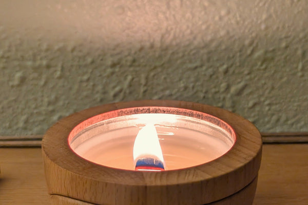 A Sero candle burning in its beech wood container on a bedside table, wick trimmed and flame steady.