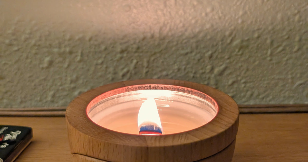 A Sero candle burning in its beech wood container on a bedside table, wick trimmed and flame steady.