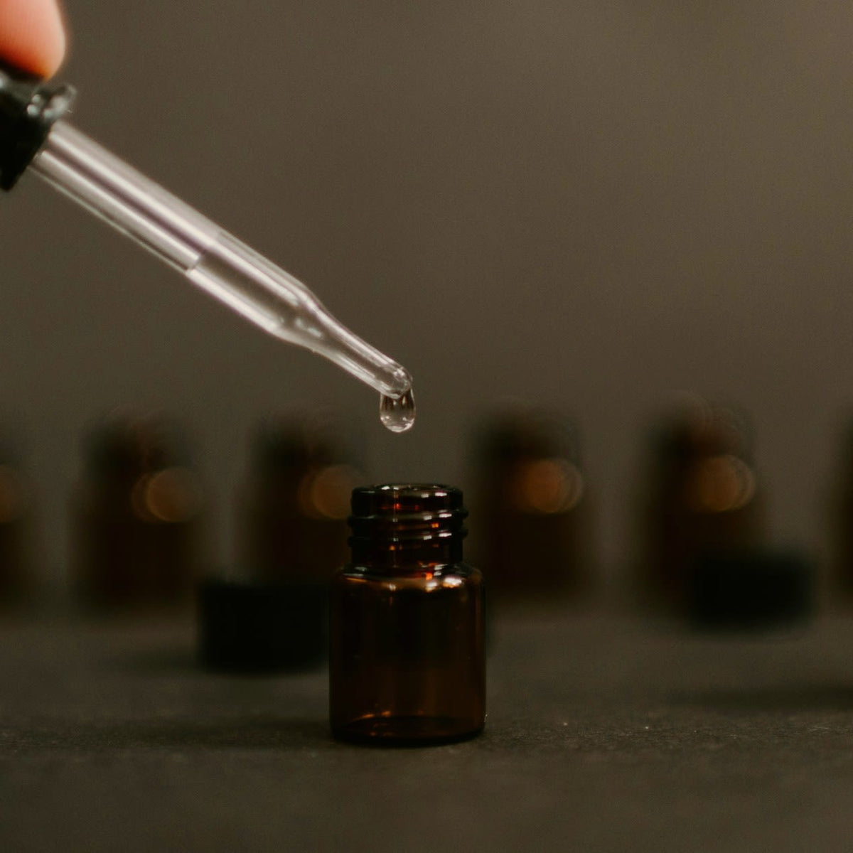 A pipette releasing a single drop above amber fragrance vials, the dose decision behind every scented candle.