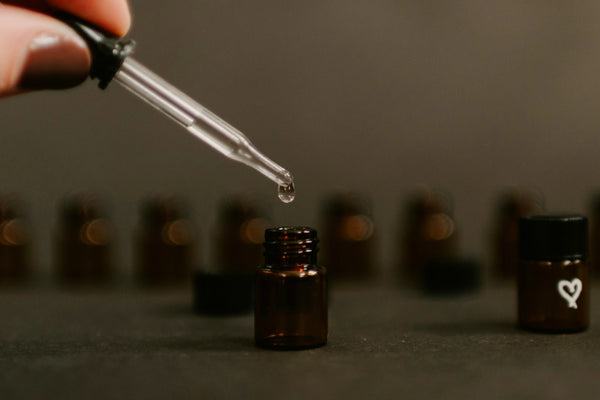 A pipette releasing a single drop above amber fragrance vials, the dose decision behind every scented candle.
