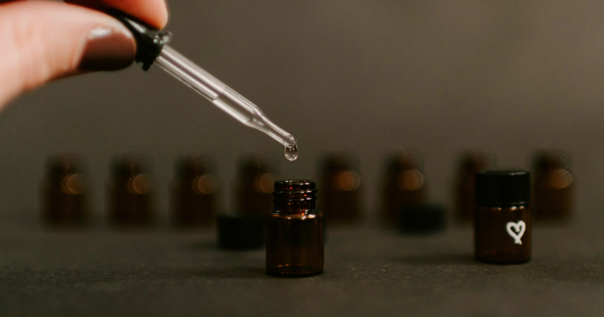 A pipette releasing a single drop above amber fragrance vials, the dose decision behind every scented candle.