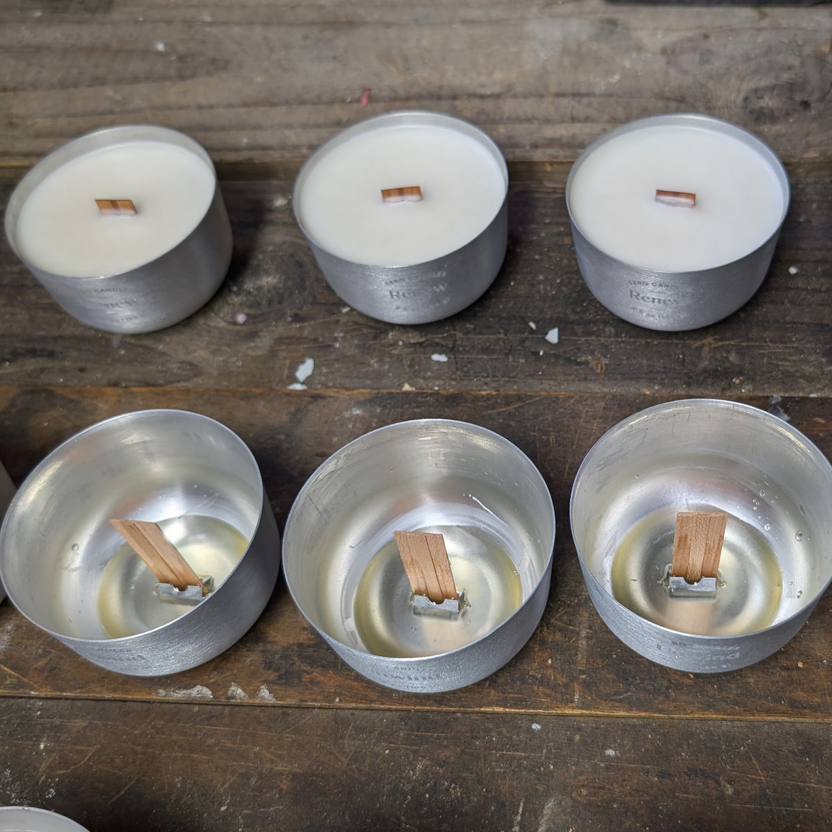 Aluminum candles on a workbench, three poured with wood wicks above three empty ones with the wood wick still in place